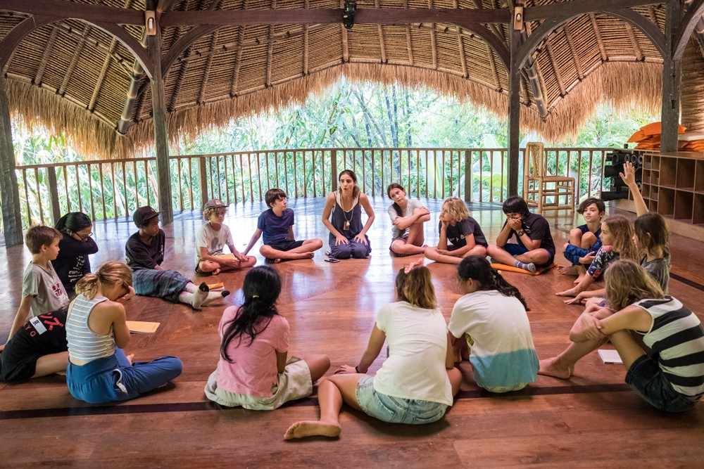 "Children sitting in a circle during an informal learning session in a bamboo classroom in Bali"