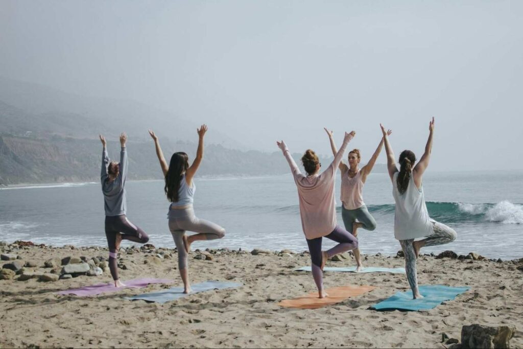 "Group beach yoga session in Bali with participants stretching towards the sky"