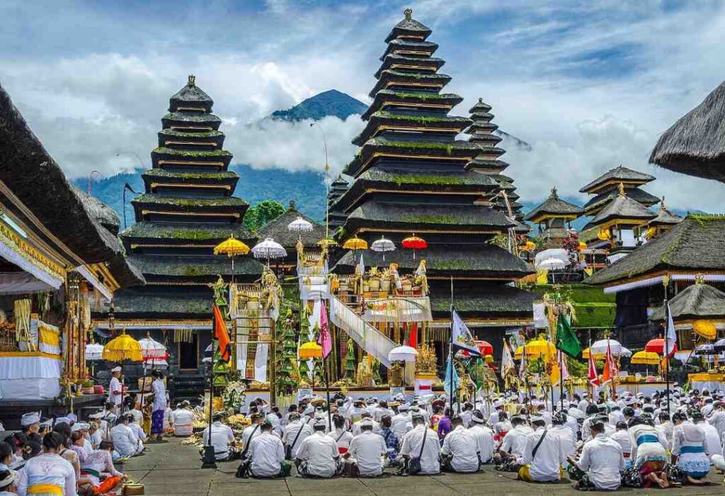 "Hindu ceremony at Besakih Temple in Bali with worshippers in white attire and decorated pagodas"